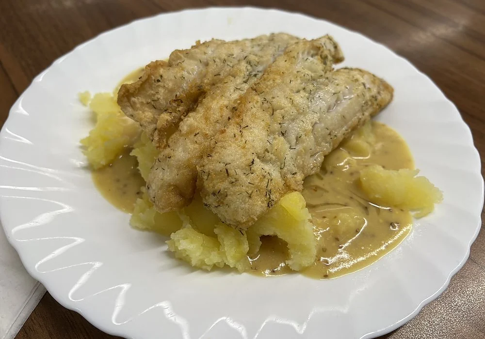 Panierte Seelachsfilets mit Kartoffeln und Senfsauce auf weißem Teller