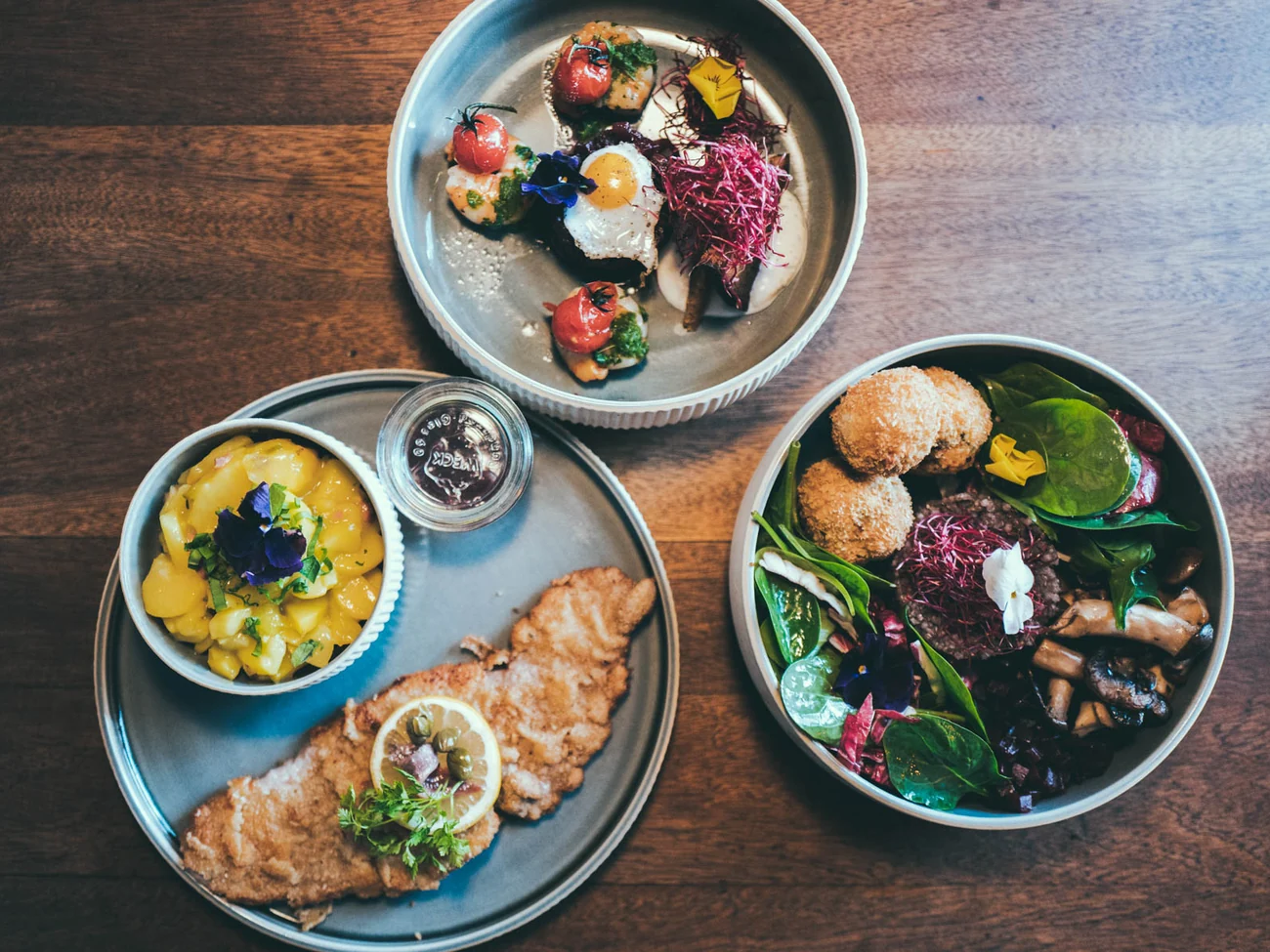 Drei Teller von oben: Schnitzel mit Kartoffelsalat, Bowl mit Ei und Schale mit Salat