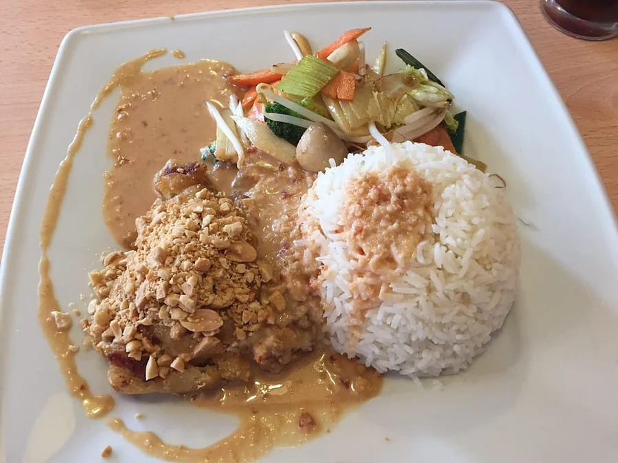 Fleisch mit Chili-Erdnuss-Sauce, Wokgemüse und Reis auf weißem Teller