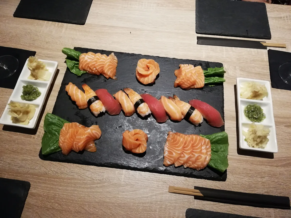Sushi und Sashimi vom Lachs und Thunfisch auf einer Schieferplatte, daneben Ingwer und Wasabi