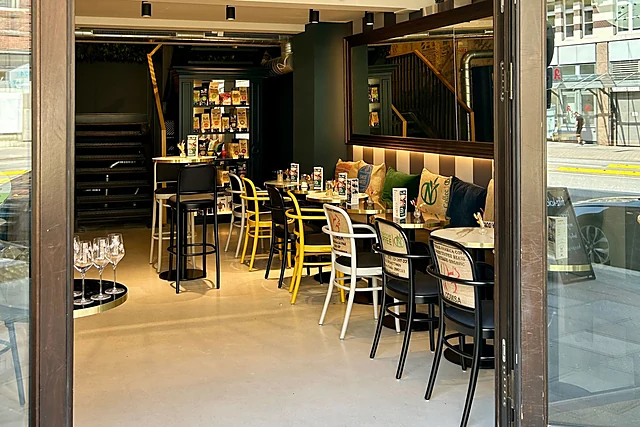 Blick durch die offene Tür in das Café mit gelben und schwarzen Stühlen, Marmortischen und Regalen mit Kaffeetüten