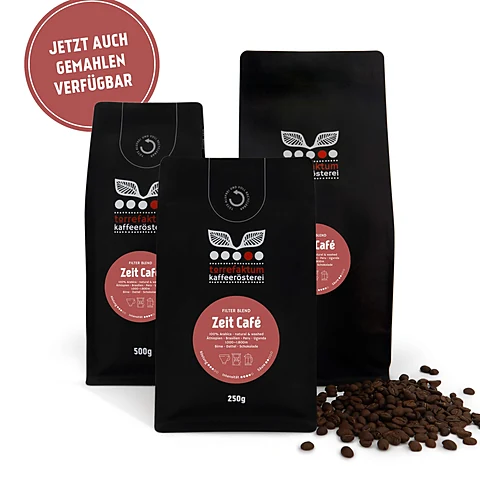 Drei schwarze Kaffeetüten mit rotem Etikett „Zeit Café“ der Torrefaktum Kaffeerösterei, daneben verstreute Bohnen