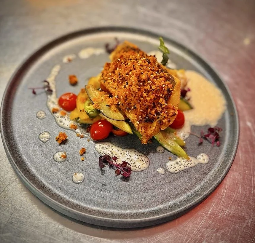 Fischfilet mit Kräuterkruste auf Zucchini, Tomaten und Schaumsauce auf grauem Teller