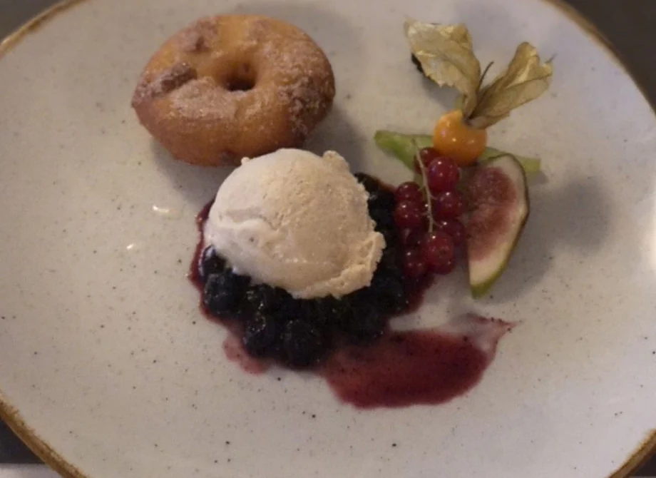 Dessert mit Krapfen, Eiskugel, Beerenkompott und Physalis auf hellem Teller