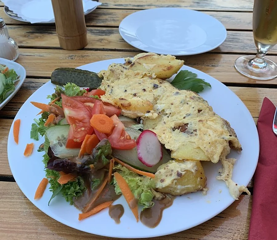 Bauernfrühstück mit Kartoffeln, Ei und Salatbeilage auf weißem Teller im Biergarten