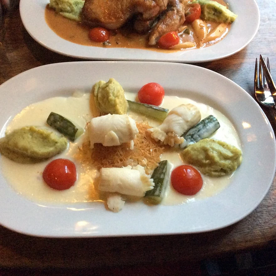 Seezungenröllchen mit Gurke, Erbsennocken und Tomaten in heller Sauce auf weißem Teller