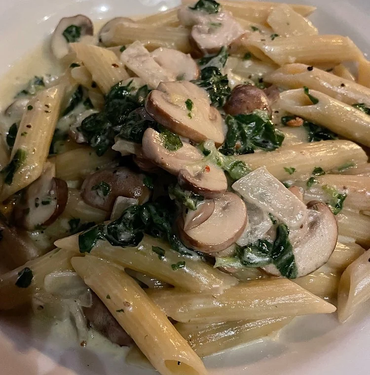 Penne mit Spinat, Champignons und Sahnesauce auf weißem Teller