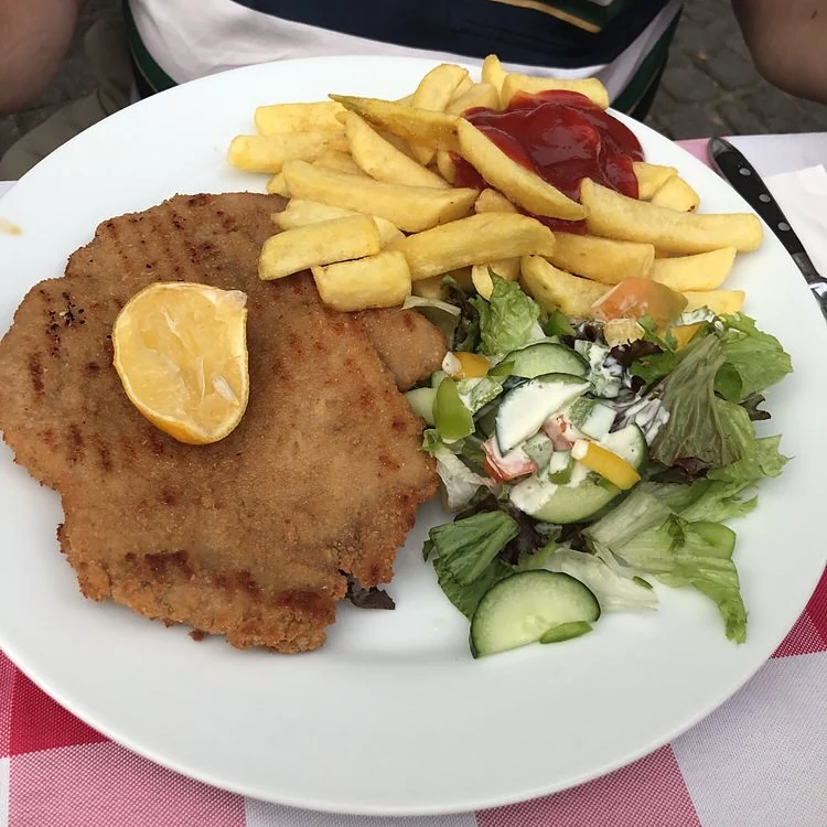 Paniertes Schnitzel mit Pommes, Zitrone und Salat auf weißem Teller